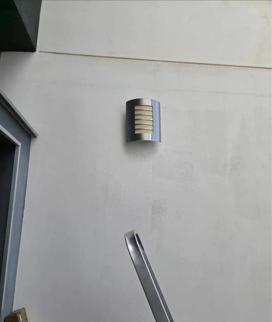 Aplique de pared antiguo, de acero inoxidable, junto a la puerta de entrada de una fachada blanca