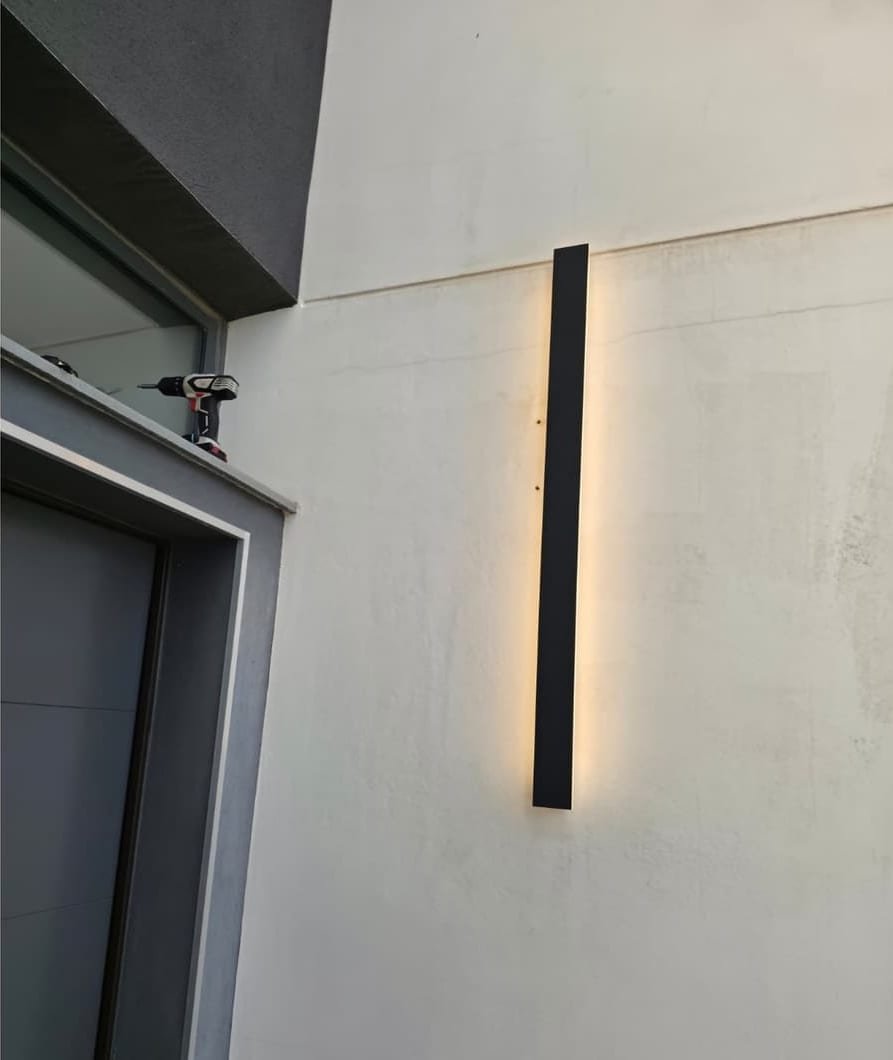 Luminaria lineal negra ya instalada y encendida en el mismo punto de la fachada