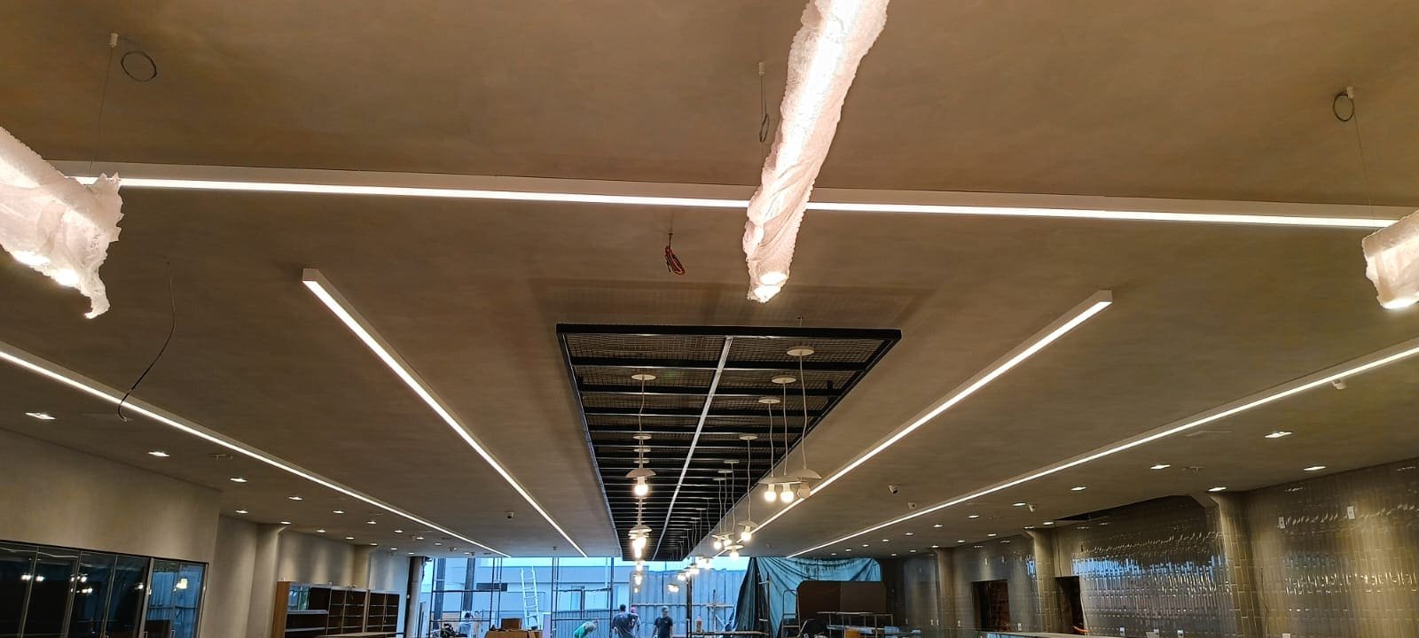 Techo de un local comercial en obra con iluminación lineal y lámparas colgantes