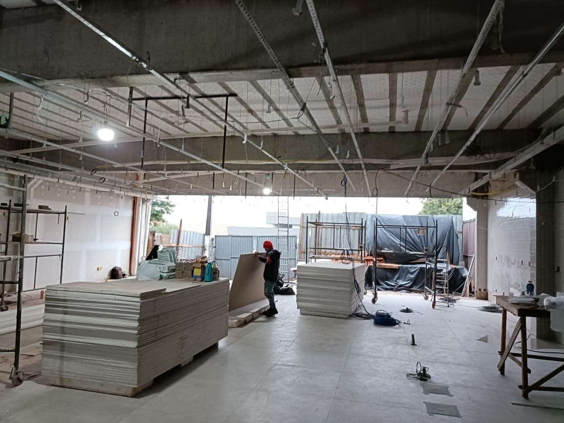 Placas de pladur apiladas en un local en obra, con operarios trabajando al fondo