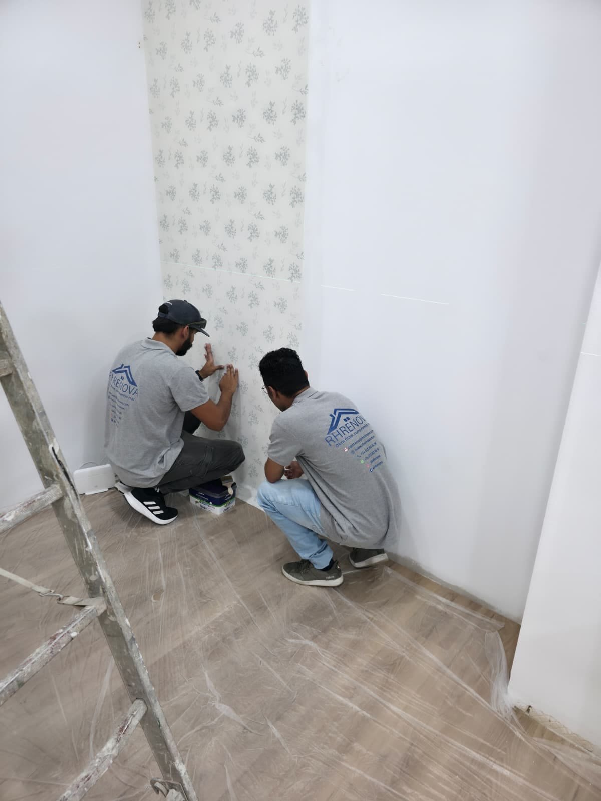 Dos operarios de RHRENOVA colocando papel pintado y alisando la unión al rodapié