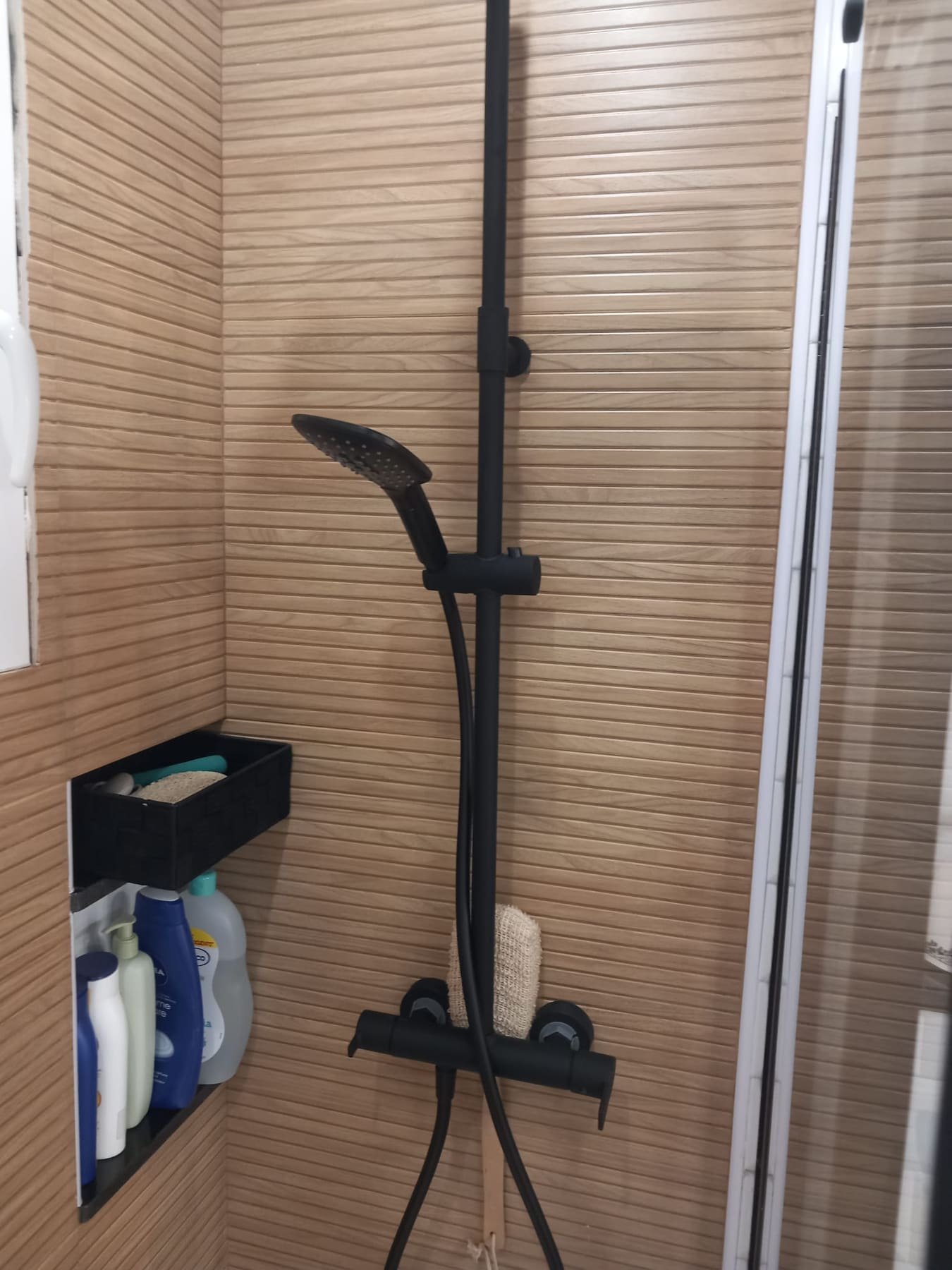 Zona de ducha alicatada en efecto madera con columna termostática negra
