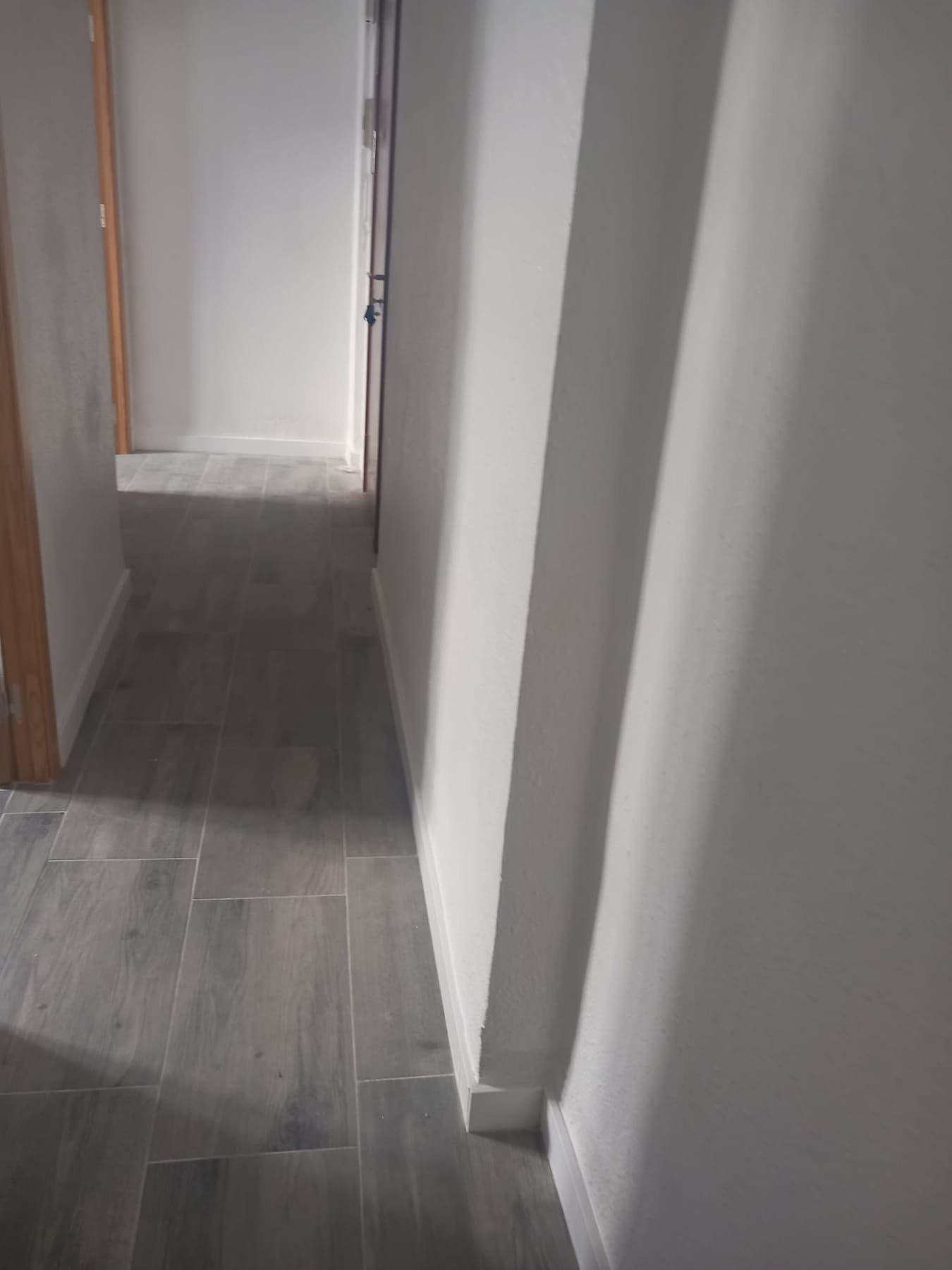 Pasillo terminado con paredes lisas pintadas en blanco y suelo efecto madera